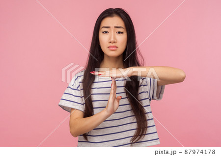 Stop, enough, I need break. Portrait of exhausted girl with long hair in t-shirt showing time-out gesture and looking imploringly, asking for pause. indoor studio shot isolated on pink background 87974178
