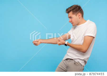 Concentrated assertive man holding invisible rope and pulling something heavy, looking motivated, metaphor of trying hard, striving to achieve goal. indoor studio shot isolated on blue background Concentrated assertive man holding invisible rope and pulling something heavy, looking motivated, metaphor of trying hard, striving to achieve goal. indoor studio shot isolated on blue background 87974455