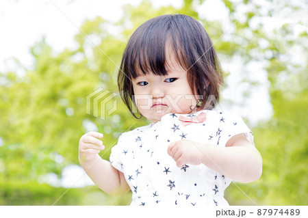 新緑の樹木を背景に怒り顔で反発する幼い女の子。成長,親離れ,教育,躾,愛情,幸せ,育児イメージ	 87974489