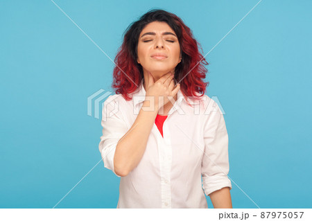 Colds and flu epidemic. Portrait of unhealthy woman with fancy red hair touching neck, suffering sore throat, feeling pain in tonsils, hard to swallow. indoor studio shot isolated on blue background Colds and flu epidemic. Portrait of unhealthy woman with fancy red hair touching neck, suffering sore throat, feeling pain in tonsils, hard to swallow. indoor studio shot isolated on blue background 87975057