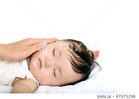 白背景で寝ている女の子の赤ちゃんの頬を撫でる母の手。愛情,家族,母性のイメージ	 87975296