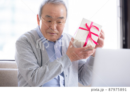 ビデオ通話　送られて来たプレゼントをオンラインで繋がった家族と一緒に開封するシニア男性 87975891