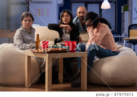 Coworkers feeling frustrated about lost video games play, doing leisure activity at office party after hours. Sad colleagues having fun with technology, beer bottles and pizza at celebration. 87975972