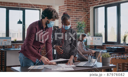 Woman expecting child and working on business project with colleague during coronavirus pandemic. Pregnant entrepreneur talking to man about growth and charts, having face mask. 87976082