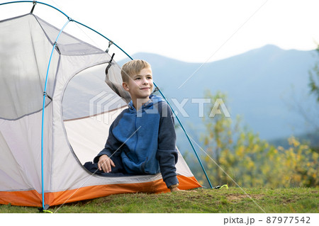 Hiker child boy resting in a tourist tent at mountain campsite enjoying view of beautiful summer nature. 87977542