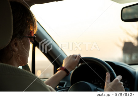 Close up view of a woman driver holding steering wheel driving a car at sunset. 87978307