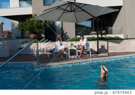 Happy family enjoys vacation in a luxury house with pool. Senior couple spends time with their son during the vacation. Selective focus  87979903