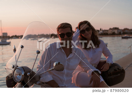 The couple enjoys a vacation while sitting on a scooter by the sea and enjoying the beautiful sunrise. Selective focus The couple enjoys a vacation while sitting on a scooter by the sea and enjoying the beautiful sunrise. Selective focus 87980020