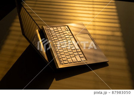A woman is typing on a laptop keyboard on a white table. The shadow from the blinds falls on the desktop. 87983050