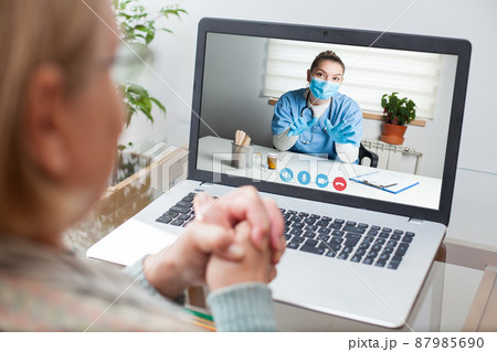 Young GP physician and elderly female patient consulting over video call 87985690