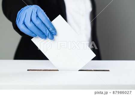Person in black suit wearing blue protective latex rubber gloves putting ballot paper in vote box Person in black suit wearing blue protective latex rubber gloves putting ballot paper in vote box 87986027