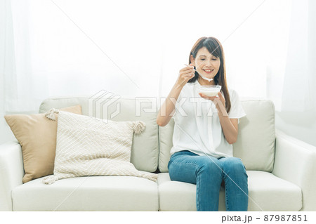ソファでヨーグルトを食べる女性（笑顔） 87987851