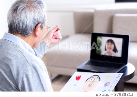 ビデオ通話　オンラインで繋がった孫に指ハートを送るシニア男性 87988812