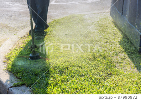 Seasonal worker man lawn mower cutting grass in roadside 87990972