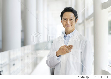胸に手を当てた白衣を着たカメラ目線で笑顔の30代の男性　医療従事者・研究者　イメージ 87991981