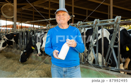 Farmer with bottle of milk in cowshed Farmer with bottle of milk in cowshed 87992495