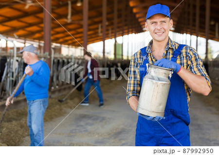 Smiling farmer standing in cowshed at dairy farm with milk churn 87992950