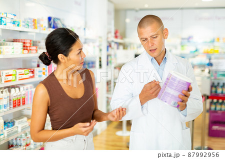 Female buyer consults the pharmacist which lotion or ointment to buy at pharmacy 87992956