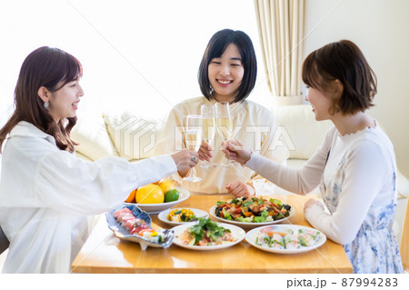 スパークリングワインを片手に、ホームパーティをする若い女性 スパークリングワインを片手に、ホームパーティをする若い女性 87994283