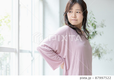 部屋着のまま腰に手を当てる体調不良の女性 87997522
