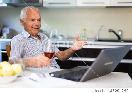 Senior man with glass of brandy and laptop Senior man with glass of brandy and laptop 88004240