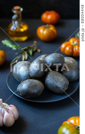 Purple potatoes with tomatoes, garlic, rosemary and olive oil on dark background Purple potatoes with tomatoes, garlic, rosemary and olive oil on dark background 88004448