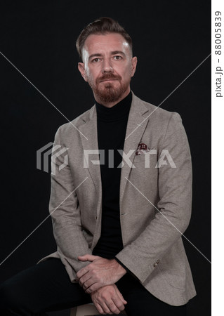Portrait of adult businessman wearing trendy suit and sitting in modern studio on stylish chair against the black background 88005839