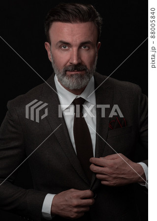 Portrait of a stylish elegant senior businessman with a beard and casual business clothes in photo studio adjusting suit 88005840
