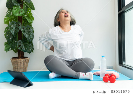 Senior Asian woman watching online courses on a laptop while exercising in the living room at home. Concept of workout training online. Senior Asian woman watching online courses on a laptop while exercising in the living room at home. Concept of workout training online. 88011679