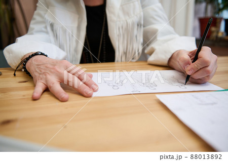 Focus on the hand of an unrecognizable fashion designer holding a pencil and drawing sketches for clothes, developing new line of dress collection Focus on the hand of an unrecognizable fashion designer holding a pencil and drawing sketches for clothes, developing new line of dress collection 88013892