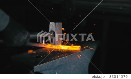 Forge workshop. Smithy manual production. Hands of smith with hammer hit on glowing hot metal, on the anvil, the forging process. Forge workshop. Smithy manual production. Hands of smith with hammer hit on glowing hot metal, on the anvil, the forging process. 88014376