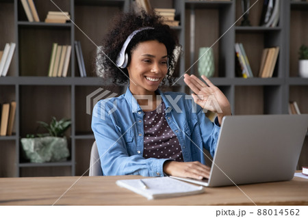 Cheerful Black student girl in wireless headphones waving hand hello 88014562