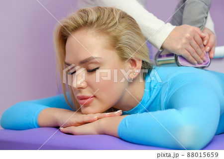 A female client receives a LPG massage in a beauty clinic. Beauty parlour. Blue suit. Lilac background. A female client receives a LPG massage in a beauty clinic. Beauty parlour. Blue suit. Lilac background. 88015659