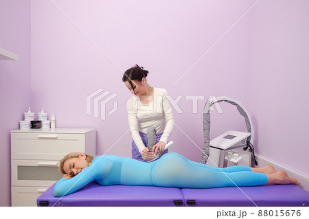 A female client receives a LPG massage in a beauty clinic. Beauty parlour. Blue suit. Lilac background. A female client receives a LPG massage in a beauty clinic. Beauty parlour. Blue suit. Lilac background. 88015676