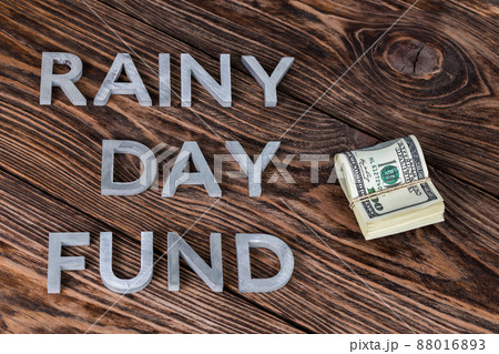 the words RAINY DAY FUND near small pack of us dollars on wooden background the words RAINY DAY FUND near small pack of us dollars on wooden background 88016893