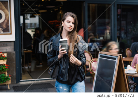 Pleasant young female with hot takeaway beverage leaving cafe Pleasant young female with hot takeaway beverage leaving cafe 88017772