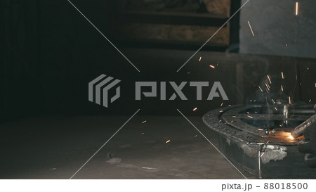 Forge workshop. Smithy. Worker in a welding hood helmet welds a part by electric welding. Sparks are reflected in the protective screen. Forge workshop. Smithy. Worker in a welding hood helmet welds a part by electric welding. Sparks are reflected in the protective screen. 88018500