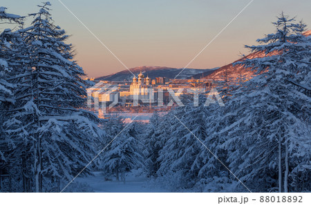 View from the winter forest to the city of Magadan. Beautiful morning landscape. Snow-covered larch trees and a large cathedral. 88018892