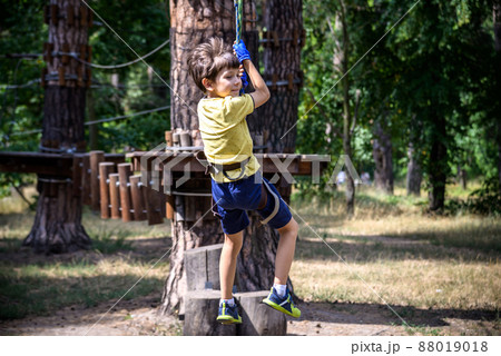 Strong excited young boy playing outdoors in rope park. Caucasian child dressed in casual clothes and sneakers at warm sunny day. Active leisure time with children concept 88019018