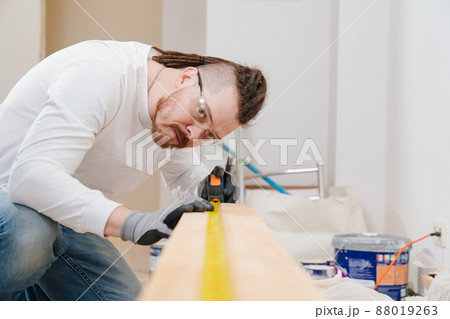 carpenter in protective gloves and glasses makes measurements on wood carpenter in protective gloves and glasses makes measurements on wood 88019263