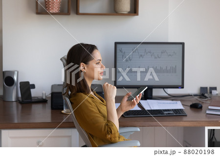 Pensive woman holds smartphone sit at workplace desk with computer Pensive woman holds smartphone sit at workplace desk with computer 88020198