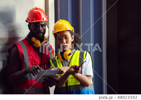 Two African american male and female worker using tablet and checking control loading freight containers from Cargo freight ship for import export. 88023502