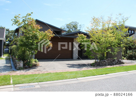 青空に映えるゆったりとしたガレージと玄関前のおしゃれで瀟洒なアースカラーの高級感のある美しい邸宅 88024166