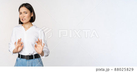 No thank you. Young disgusted asian woman declining proposal, shaking hands and step back, looking with dislike, rejecting offer, standing over white background 88025829