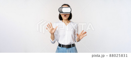 Amazed young woman in virtual reality, using vr glasses headset, standing over white background Amazed young woman in virtual reality, using vr glasses headset, standing over white background 88025831