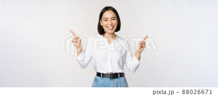 Image of beautiful asian woman pointing fingers left and right, making decision, showing two variants choices, standing over white background 88026671