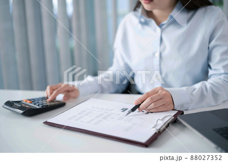 Portrait of  Asian Business woman working from office taking reading and writing notes in note pad working on laptop computer  in her workstation 88027352