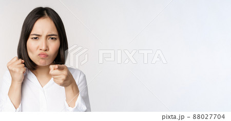 Close up of angry young woman clench fists, ready for fight, fighting, standing over white background 88027704