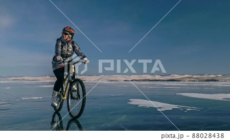 Woman is riding bicycle on the ice. Tires on bike are covered wi 88028438