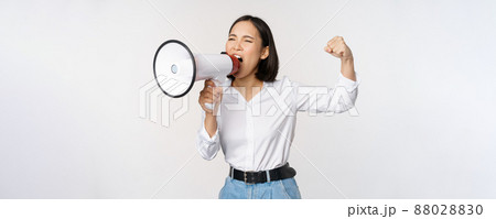 Enthusiastic asian woman, girl activist shouting at protest, using megaphone, looking confident, talking in loudspeaker, protesting, standing over white background Enthusiastic asian woman, girl activist shouting at protest, using megaphone, looking confident, talking in loudspeaker, protesting, standing over white background 88028830